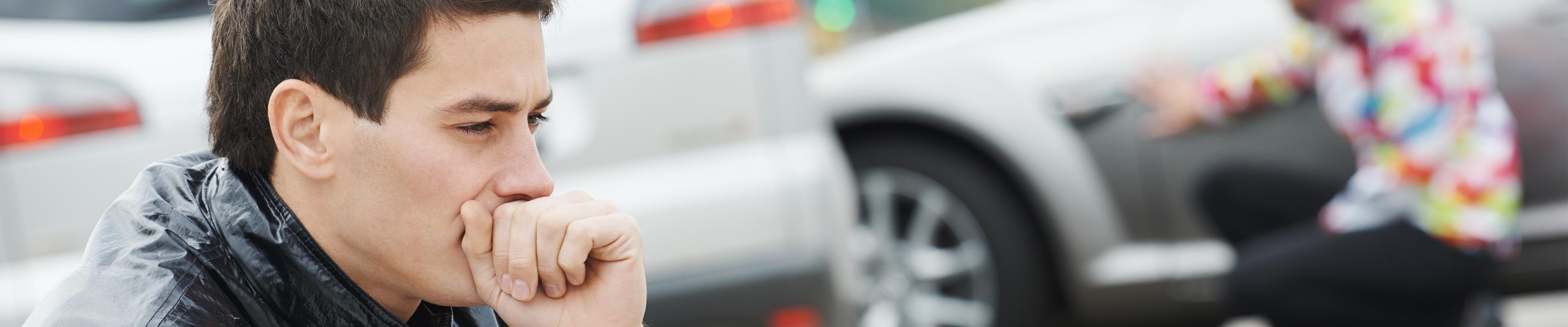 man sitting in front of a car accident looking worried