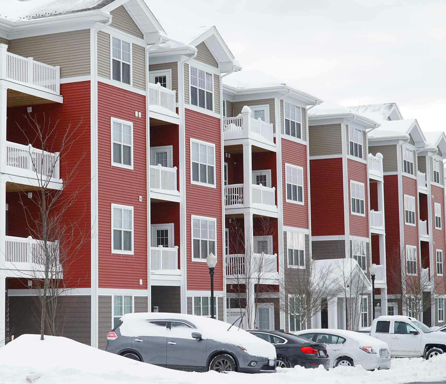 Red and tan apartment complex in winter with snow on roof.