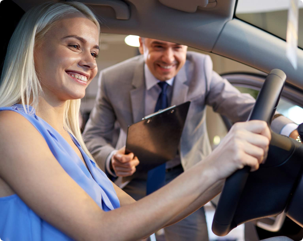A white blonde woman smiles at her new car while the male salesman stands outside with a clipboard to help her insure the financed car.
