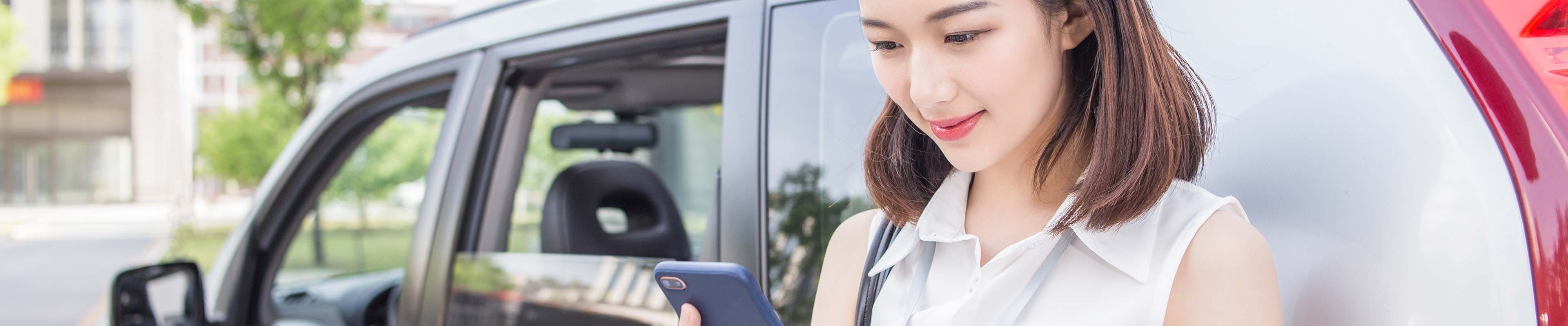 Driver Looking at her phone leaning against her car Web